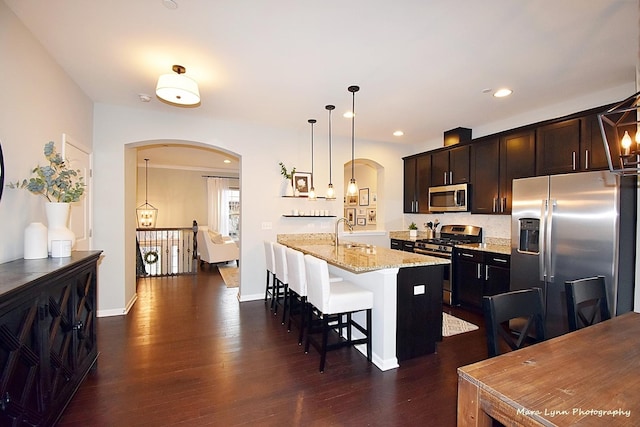 kitchen with light stone countertops, appliances with stainless steel finishes, a kitchen island with sink, decorative light fixtures, and a breakfast bar