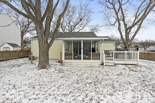 snow covered back of property with a wooden deck, a sunroom, and central air condition unit