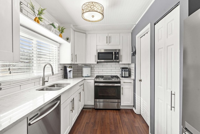 kitchen with appliances with stainless steel finishes, dark hardwood / wood-style floors, white cabinetry, sink, and light stone counters