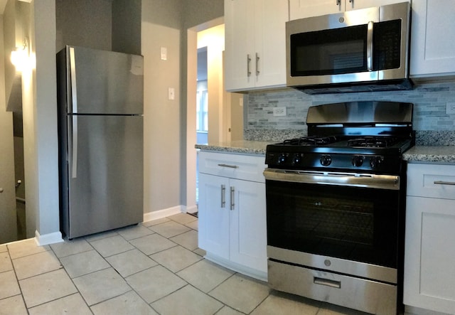 kitchen with tasteful backsplash, white cabinetry, light stone countertops, light tile patterned flooring, and stainless steel appliances