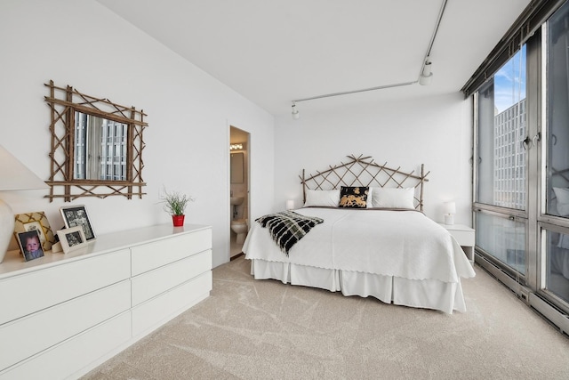 bedroom with rail lighting, a baseboard heating unit, ensuite bath, and light carpet