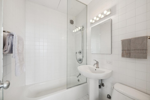 bathroom featuring toilet, tiled shower / bath, and tile walls