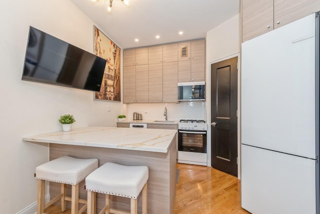 kitchen with kitchen peninsula, sink, white appliances, light hardwood / wood-style floors, and a breakfast bar area