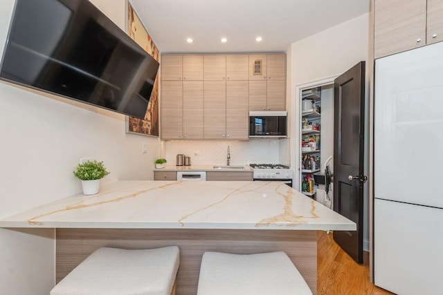 kitchen with a kitchen bar, backsplash, white appliances, and sink