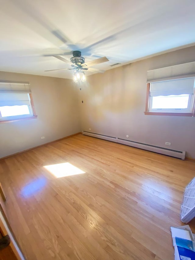 spare room featuring ceiling fan, a baseboard heating unit, a healthy amount of sunlight, and light wood-type flooring