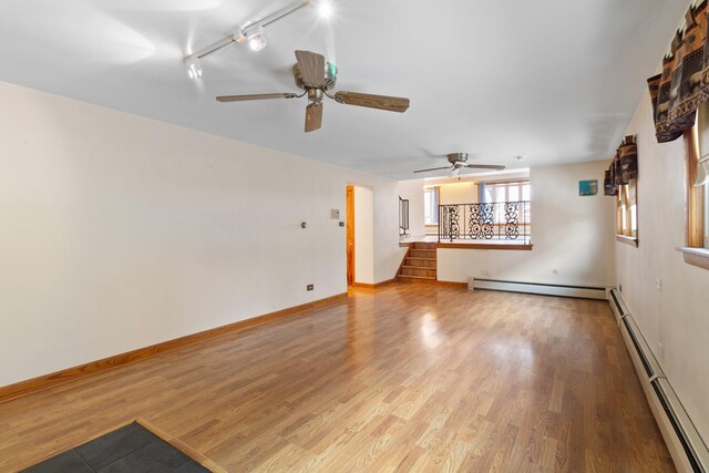 unfurnished living room featuring ceiling fan, a baseboard radiator, hardwood / wood-style floors, and a wood stove