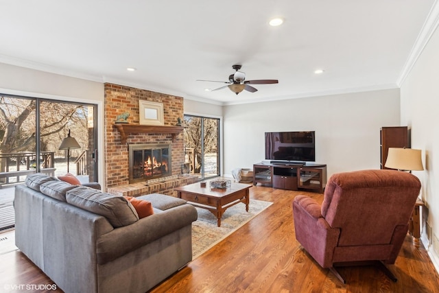 living room with crown molding, hardwood / wood-style flooring, ceiling fan, and a brick fireplace