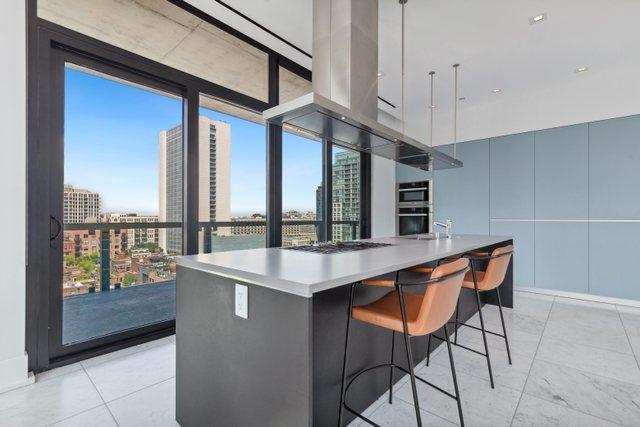 kitchen featuring decorative light fixtures, a large island with sink, expansive windows, and stainless steel double oven