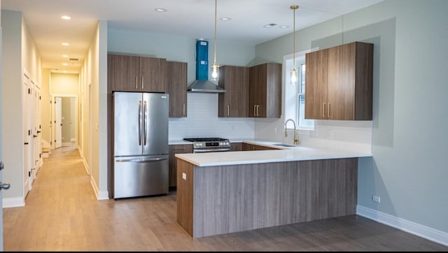 kitchen with wall chimney range hood, stainless steel appliances, tasteful backsplash, light hardwood / wood-style floors, and kitchen peninsula