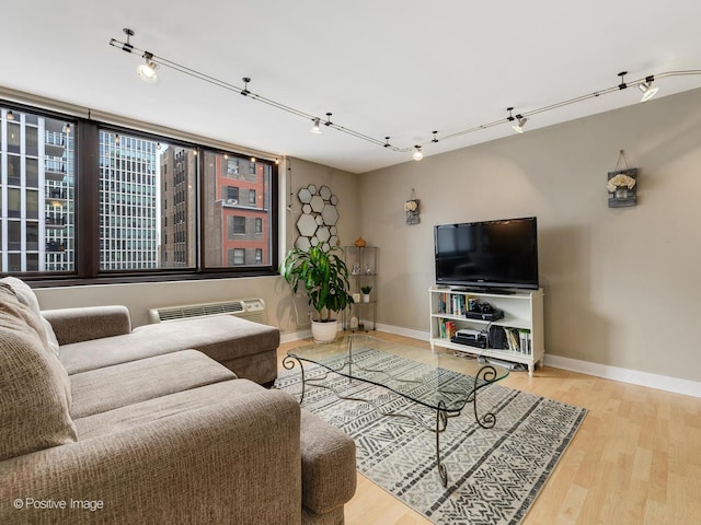 living room featuring a wall unit AC, wood finished floors, rail lighting, and baseboards