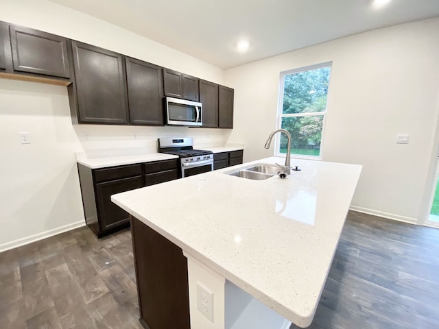 kitchen featuring appliances with stainless steel finishes, sink, a kitchen island with sink, dark wood-type flooring, and dark brown cabinets