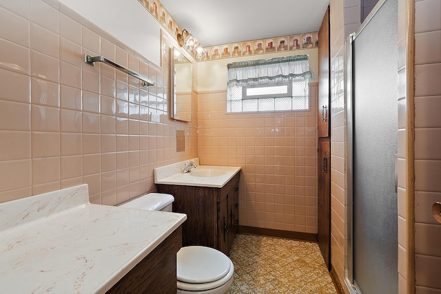 bathroom featuring a shower with door, toilet, vanity, and tile walls