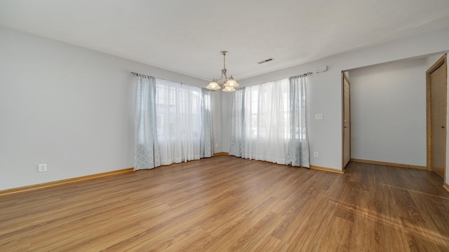 empty room featuring a notable chandelier and light hardwood / wood-style flooring