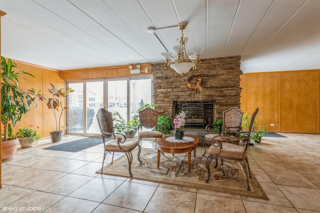 tiled living room featuring an inviting chandelier, a stone fireplace, and wooden walls