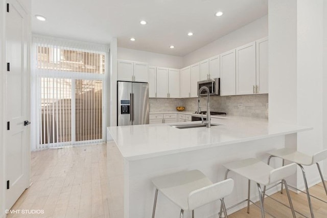 kitchen featuring stainless steel appliances, a breakfast bar, white cabinets, and kitchen peninsula