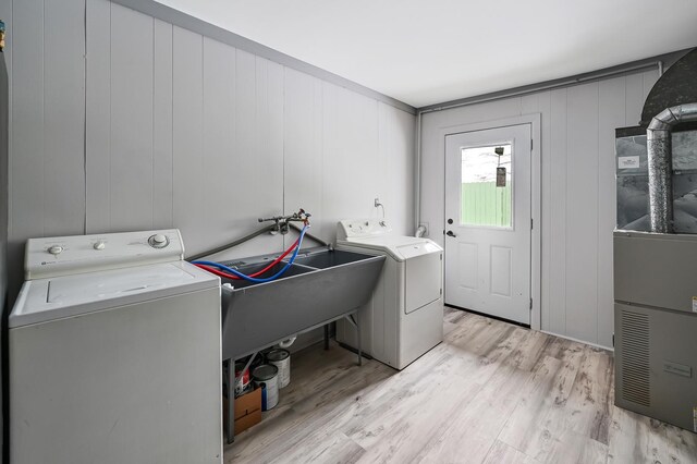 washroom with wooden walls, heating unit, washing machine and dryer, and light wood-type flooring