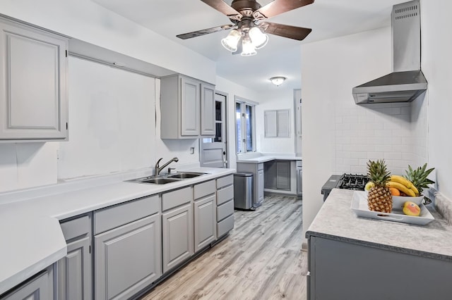 kitchen featuring sink, wall chimney range hood, gray cabinetry, and light wood-type flooring