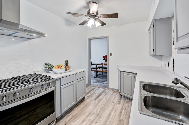 kitchen with stainless steel gas stove, wall chimney exhaust hood, sink, light wood-type flooring, and gray cabinetry