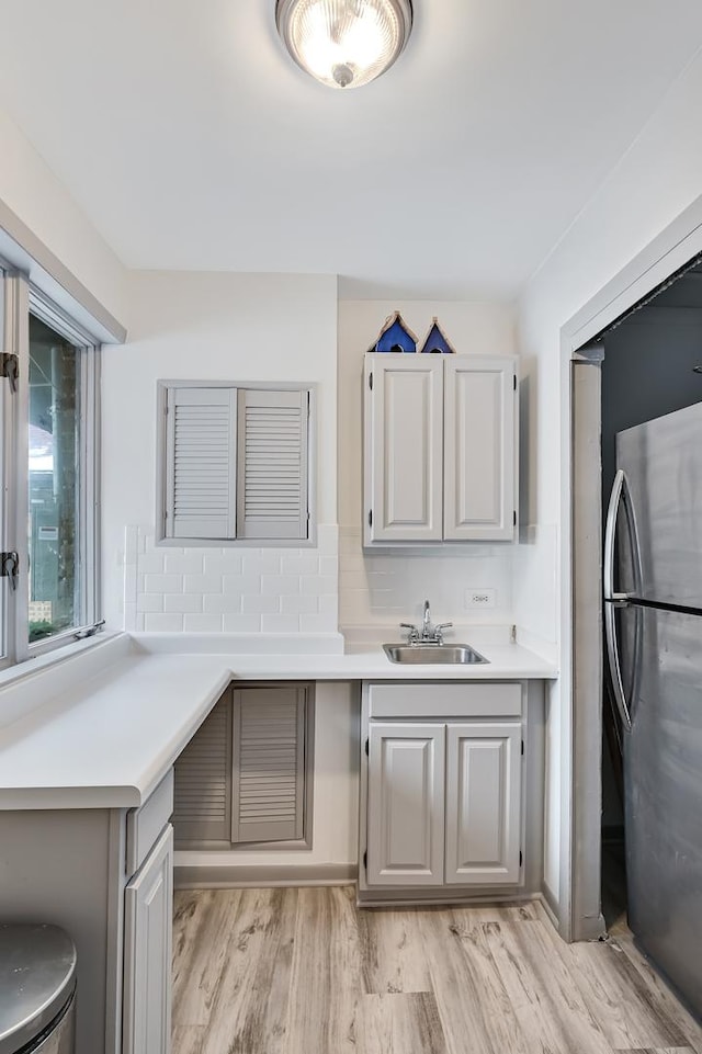 kitchen with tasteful backsplash, stainless steel refrigerator, sink, light wood-type flooring, and gray cabinets