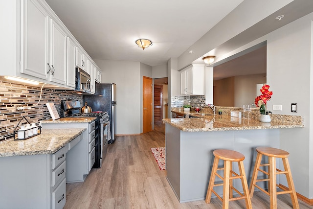 kitchen with white cabinetry, light stone counters, a breakfast bar area, and stainless steel appliances