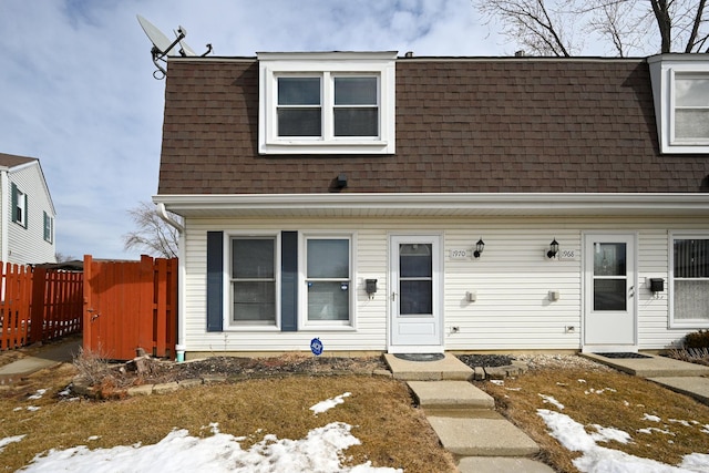 view of front of home with mansard roof, roof with shingles, and fence