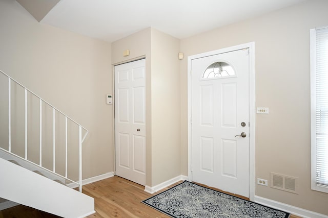 entrance foyer featuring baseboards, visible vents, stairway, wood finished floors, and a healthy amount of sunlight