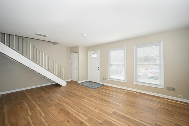 foyer entrance with light wood-type flooring, stairway, baseboards, and visible vents