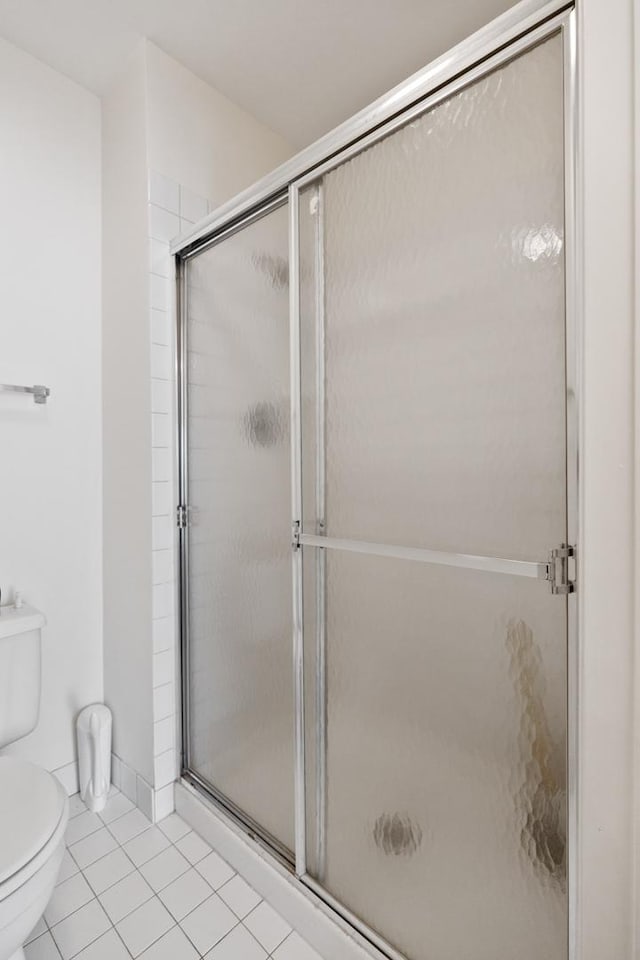 bathroom with tile patterned floors, toilet, and a shower with door