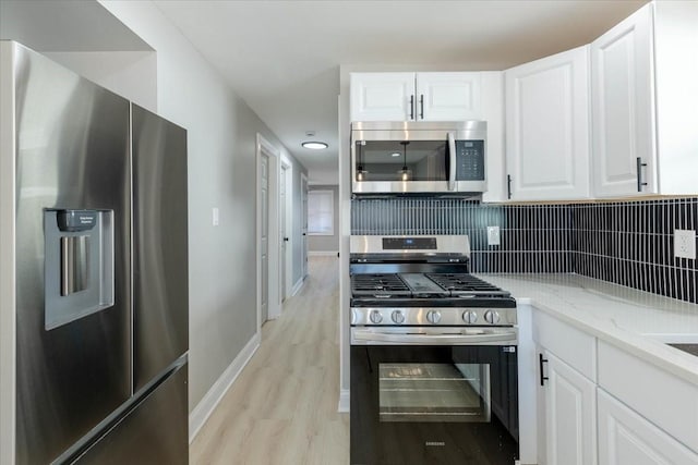 kitchen with light stone countertops, appliances with stainless steel finishes, white cabinets, and light wood-type flooring