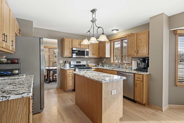 kitchen with pendant lighting, light hardwood / wood-style flooring, appliances with stainless steel finishes, light stone countertops, and a kitchen island