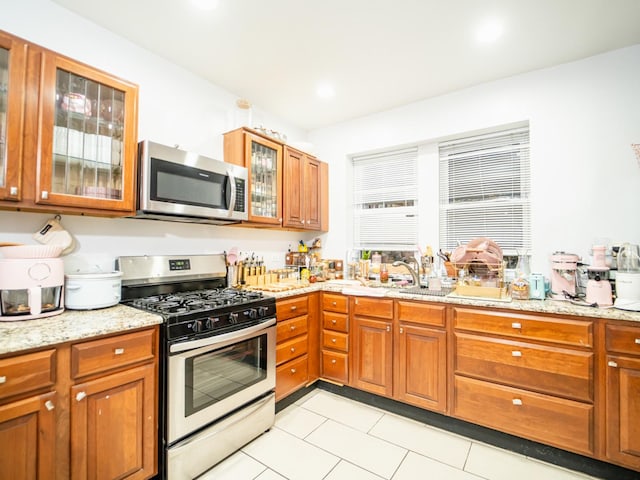 kitchen featuring sink, light stone counters, light tile patterned floors, and appliances with stainless steel finishes