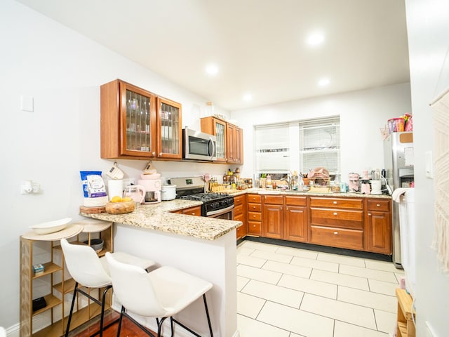 kitchen with light stone countertops, appliances with stainless steel finishes, light tile patterned floors, kitchen peninsula, and a breakfast bar