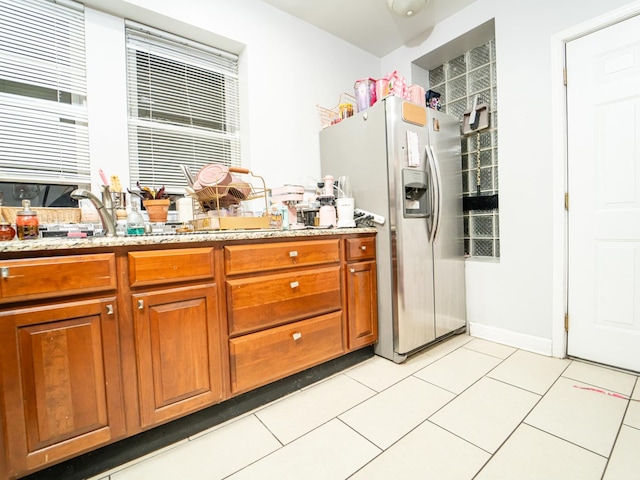 kitchen with light stone countertops, light tile patterned floors, stainless steel fridge with ice dispenser, and sink