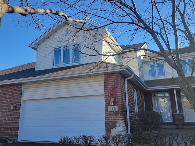 view of side of property with a garage, brick siding, and roof with shingles