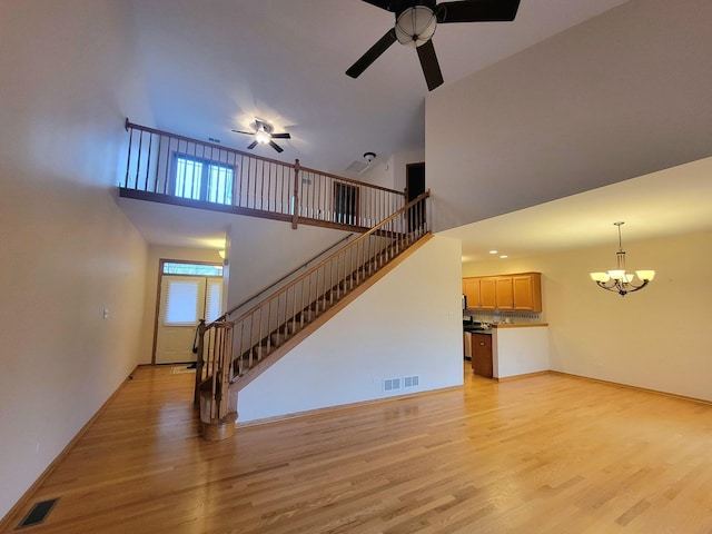 unfurnished living room featuring ceiling fan with notable chandelier, stairway, light wood-type flooring, and visible vents