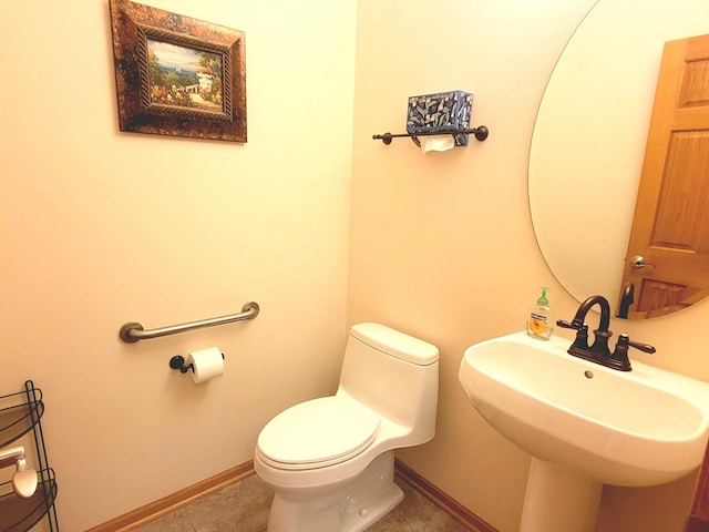 half bath featuring baseboards, a sink, toilet, and tile patterned floors