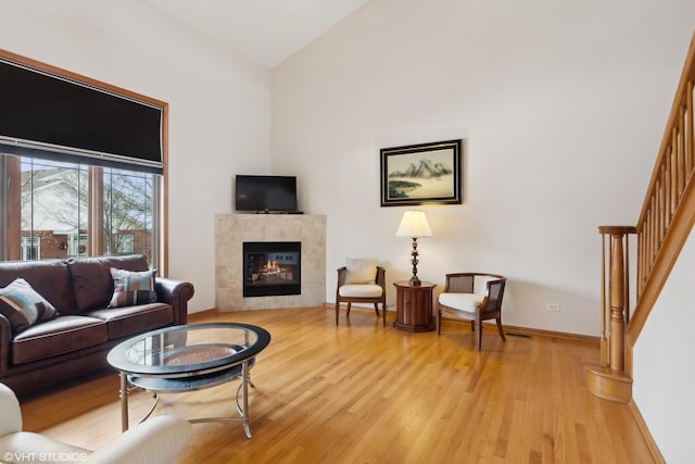 living area featuring lofted ceiling, a tile fireplace, baseboards, light wood-style floors, and stairway