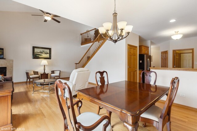 dining space featuring a tile fireplace, ceiling fan with notable chandelier, and light hardwood / wood-style floors