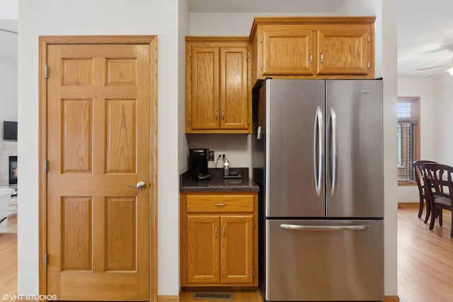 kitchen with dark stone counters, light wood finished floors, brown cabinetry, and freestanding refrigerator