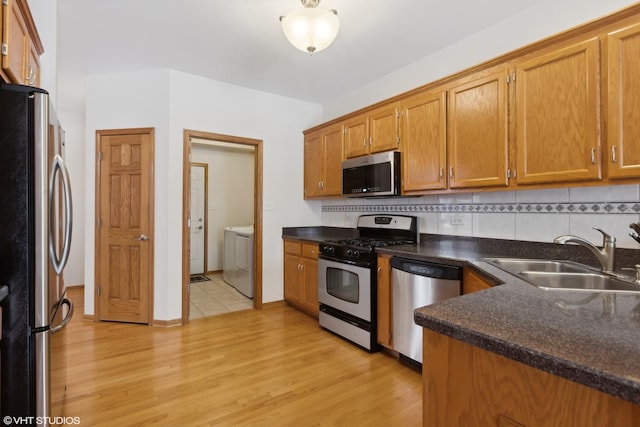 kitchen with tasteful backsplash, appliances with stainless steel finishes, sink, and light hardwood / wood-style flooring