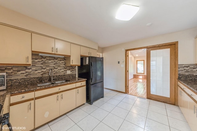 kitchen with tasteful backsplash, dark stone countertops, sink, black fridge, and cream cabinets