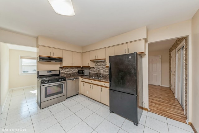 kitchen with appliances with stainless steel finishes, sink, cream cabinets, light tile patterned flooring, and decorative backsplash