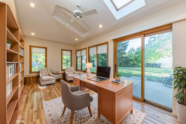 home office with ceiling fan, lofted ceiling with skylight, and light hardwood / wood-style flooring