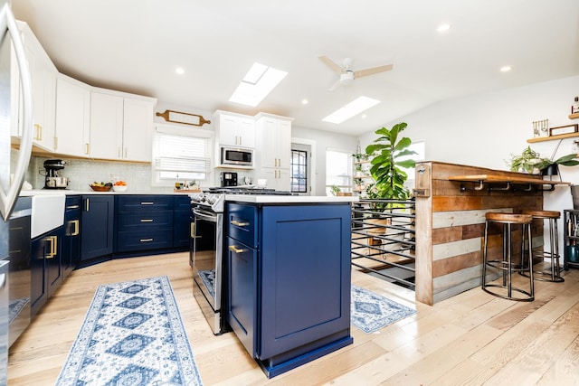 kitchen with lofted ceiling with skylight, blue cabinets, white cabinetry, a center island, and stainless steel appliances