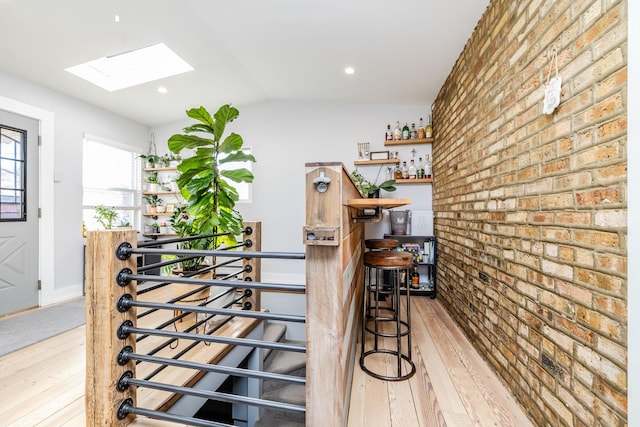 bar featuring lofted ceiling with skylight, light hardwood / wood-style floors, and brick wall