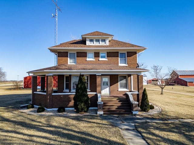 american foursquare style home featuring a porch, a front lawn, a shingled roof, and brick siding