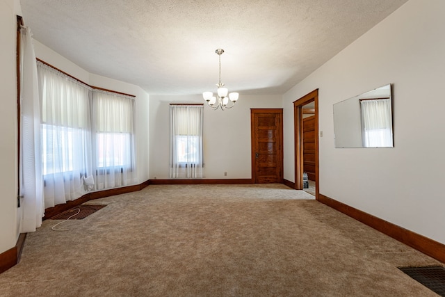 unfurnished room with baseboards, visible vents, a textured ceiling, carpet flooring, and a chandelier