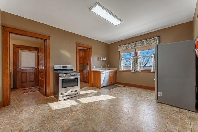 kitchen with baseboards, brown cabinetry, appliances with stainless steel finishes, light countertops, and a sink