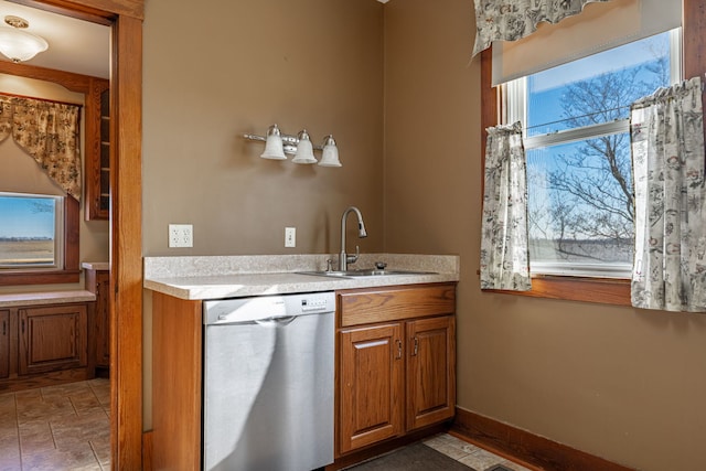 kitchen with light countertops, stainless steel dishwasher, brown cabinetry, a sink, and baseboards