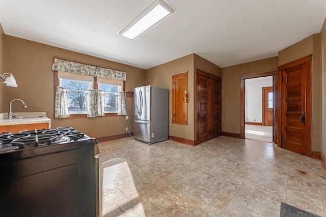 kitchen featuring stainless steel refrigerator with ice dispenser, light countertops, black gas range oven, a sink, and baseboards